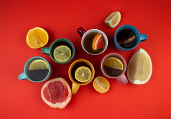 Many mugs of tea and citrus fruits on a red background, top view. Lemon, pomelo, orange, citrus Sweetie, grapefruit.