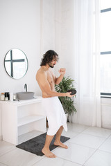 Young shirtless man with portable wireless bluetooth speaker dancing in bathroom