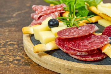 Meat and cheese plate antipasti snack with Prosciutto ham, Parmesan, Blue cheese, Cantaloupe melon and Olives on olive wood serving board on dark stone background