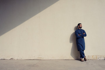 Young man with beard wearing blue long traditional cloth standing at wall wtih sunlight and shadow background, Isolated.