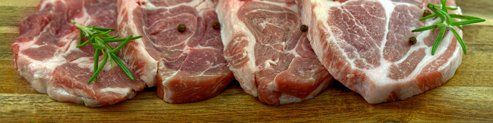raw pork steak on black stone and wood. Pork with spices: rosemary and pepper. Close-up raw pork steaks. panoramic