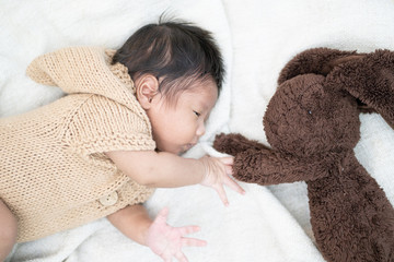 Adorable newborn baby peacefully sleeping with brown rabbit doll on a white blanket.