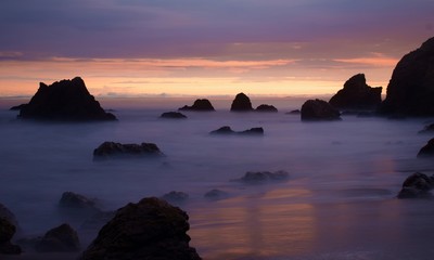 Rocks in sea, clouds against sky during sunset