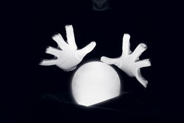 Spiritual session predicting the future. Open hands in white gloves over a luminous crystal ball.