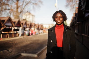 Portrait of a curly haired african woman wearing fashionable black coat and red turtleneck posing...