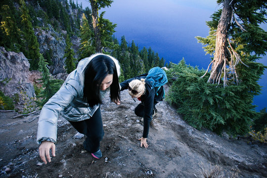 Two hikers helping each other in the mountains adjacent to a blue lake