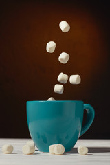 Marshmallow falls into a mug of hot cocoa chocolate drink on a dark background: the concept of winter food and drink, and flying marshmallows