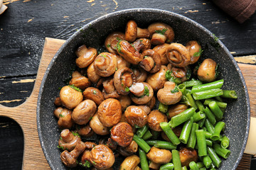 Frying pan with tasty cooked mushrooms and green beans on table
