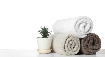 Fototapeta na wymiar Rolled clean towels for bathroom and houseplant on table against white background. Space for text