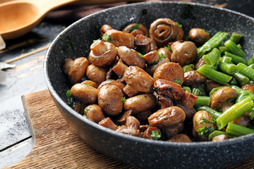 Frying pan with tasty cooked mushrooms and green beans on table