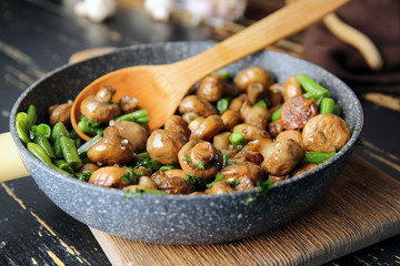 Frying pan with tasty cooked mushrooms and green beans on table