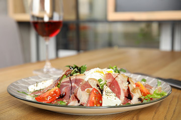 Delicious prosciutto salad with vegetables served on wooden table indoors. Space for text