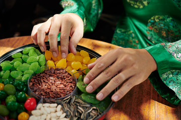 Hands of Vietnamese man in traditional costume taking dried snacks from mut plate