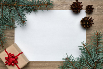 Fototapeta na wymiar Christmas or New Year background. White sheet of paper with copy space, gift box and Christmas tree branches on wood. Flat lay, view from above