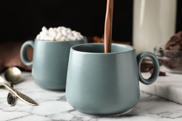 Pouring hot cocoa drink into cup on white marble table