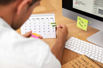 Man putting sticker on calendar at table in office, closeup