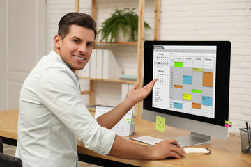 Fototapeta na wymiar Handsome man using calendar app on computer in office