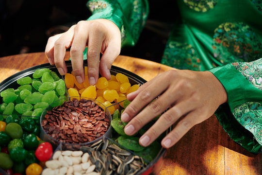 Hands of Vietnamese man in traditional costume taking dried snacks from mut plate