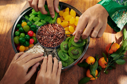Hands of people taking seeds and dried fruits and berries from good luck food tray served for Lunar New Year celebration