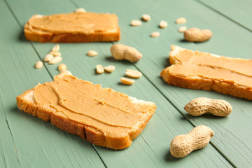 Slices of bread with tasty peanut butter on color wooden background