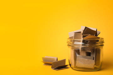 Glass jar full of brown paper sheets on yellow background, space for text