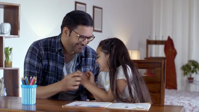 Young Indian father tickling his daughter and making her laugh hard. 4k Stock Footage of an Indian father making his daughter laugh by tickling her sitting on the study table. Family time with kids...