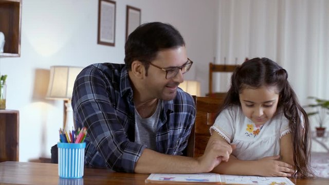 Indian father and his cute little daughter reading a story book and spending quality time. HD Stock Video of a man helping his happy-go-lucky daughter with her studies. Indian father explaining hom...