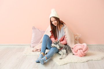 Young woman with funny husky puppy sitting near color wall