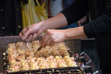 Vendor making takoyaki on a takoyaki pan in Osaka, Japan.