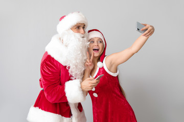 Young couple dressed as Santa taking selfie on light background