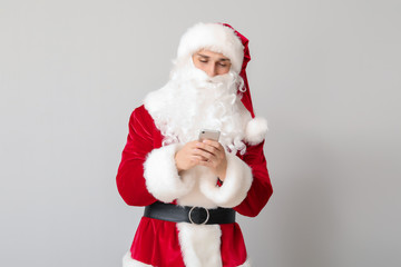 Fototapeta na wymiar Young man in Santa costume and with mobile phone on light background