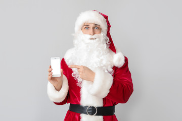 Young man in Santa costume and with mobile phone on light background