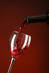 Fototapeta na wymiar Pouring of wine into glass on color background