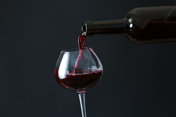 Fototapeta na wymiar Pouring of wine into glass on dark background