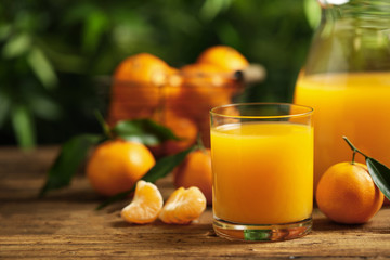 Glass and bottle of fresh tangerine juice and fruits on wooden table