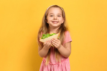 Cute little girl with tasty sandwich on yellow background
