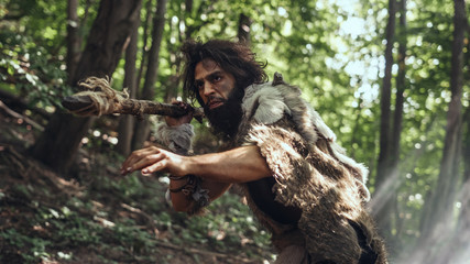 Portrait of Primeval Caveman Wearing Animal Skin and Fur Hunting with a Stone Tipped Spear in the Prehistoric Forest. Prehistoric Neanderthal Hunter Scavenging with Primitive Tools in the Jungle