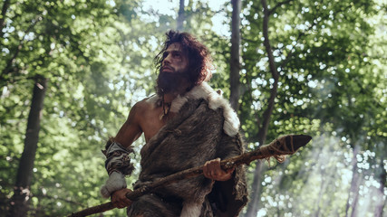 Portrait of Primeval Caveman Wearing Animal Skin and Fur Hunting with a Stone Tipped Spear in the Prehistoric Forest. Prehistoric Neanderthal Hunter Ready to Throw Spear in the Jungle