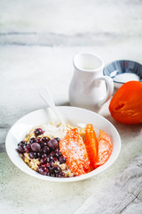 Fototapeta na wymiar Oatmeal with persimmons, coconut and berries in a white plate, copy space