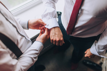 A man, a friend helps fasten the sleeves and cufflink to the groom. Hands of two men close-up. Morning and preparation of the groom. Wedding, holiday, photography.