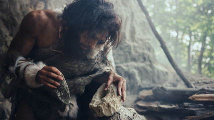 Closeup Shot of Primeval Caveman in Animal Skin Hits Rock with Sharp Stone, Makes First Primitive...