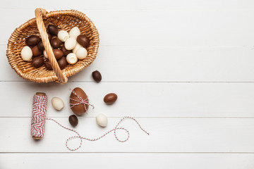 Basket with chocolate Easter eggs on white wooden background