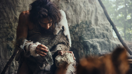 Close-up Shot of a Primeval Caveman Wearing Animal Skin Hits Rock with Sharp Stone, Makes First...