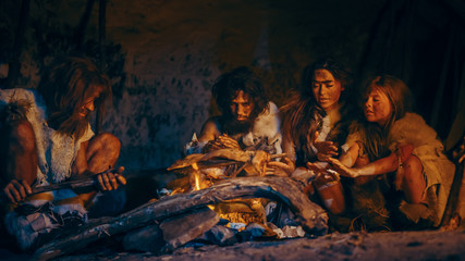 Neanderthal or Homo Sapiens Family Cooking Animal Meat over Bonfire and then Eating it. Tribe of...