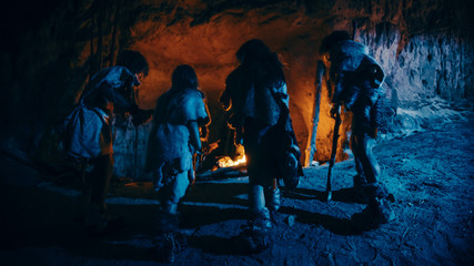 Tribe of Prehistoric Hunter-Gatherers Wearing Animal Skins Live in a Cave at Night. Neanderthal or...