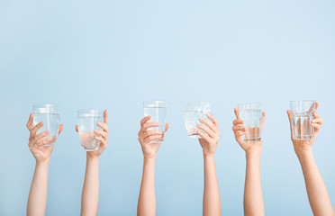 Female hands with glasses of water on color background
