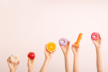 Female hands with sweet donuts, carrot and orange on color background