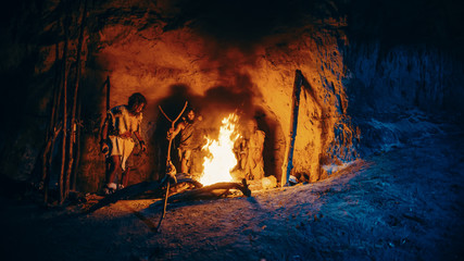 Tribe of Prehistoric Hunter-Gatherers Wearing Animal Skins Stand Around Bonfire Outside of Cave at...