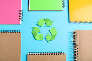 Recycling symbol, plastic and paper notebooks on light blue background, flat lay