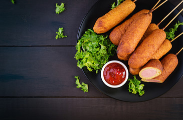 Traditional American corn dogs with mustard and ketchup on black plate. Street food. Top view, copy space